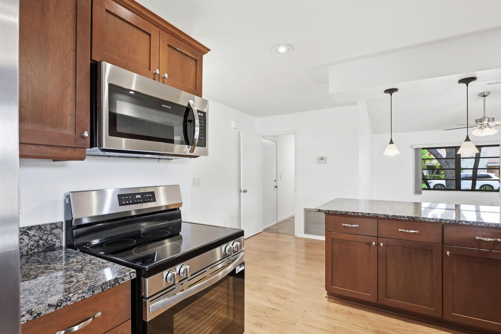 A kitchen features wood cabinets, granite countertops, stainless steel appliances, and light wood flooring — 7909 NW 18th Place, Margate FL 33063, MARGATE, FL