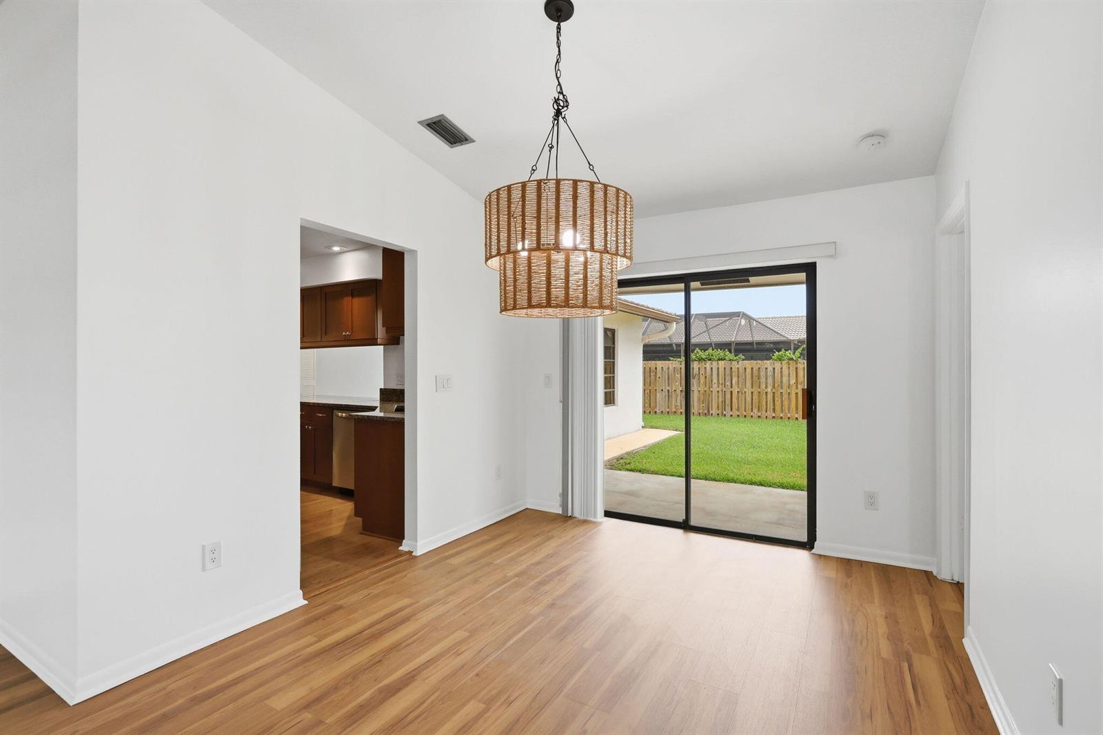 A dining area with wood-look flooring, a tiered woven chandelier, and sliding glass patio doors — 7909 NW 18th Place, Margate FL 33063, MARGATE, FL