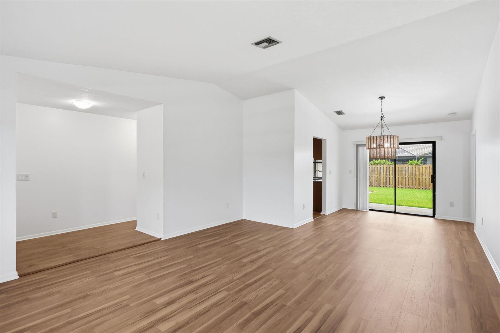 An open-concept living area features light wood-look flooring, white walls, and a sliding glass door — 7909 NW 18th Place, Margate FL 33063, MARGATE, FL