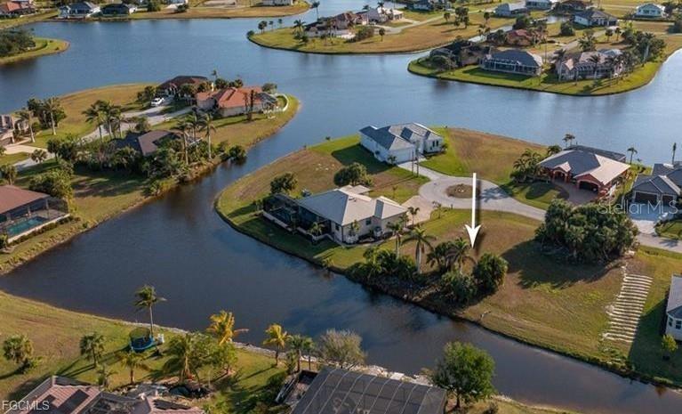 An aerial view shows a vacant waterfront lot marked by an arrow in a residential neighborhood — 16219 CAYMAN LANE, PUNTA GORDA, FL