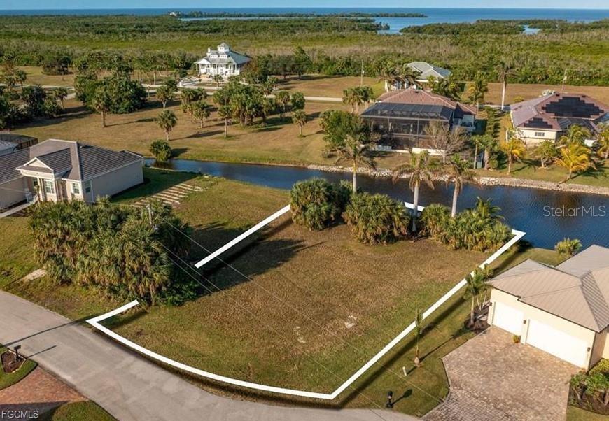An aerial view shows a vacant, grassy residential lot bordered by a canal and houses — 16219 CAYMAN LANE, PUNTA GORDA, FL