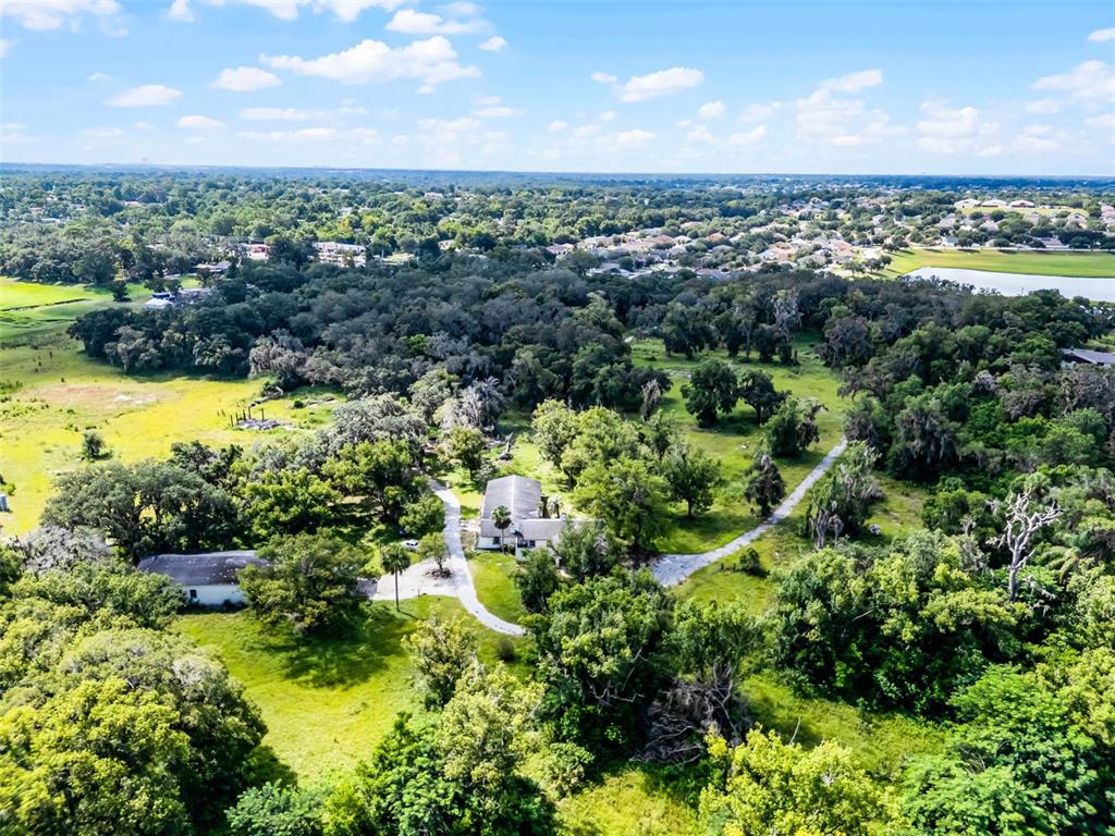 An aerial view shows two buildings surrounded by dense trees and open grassy fields — 7625 CLARCONA OCOEE ROAD, ORLANDO, FL