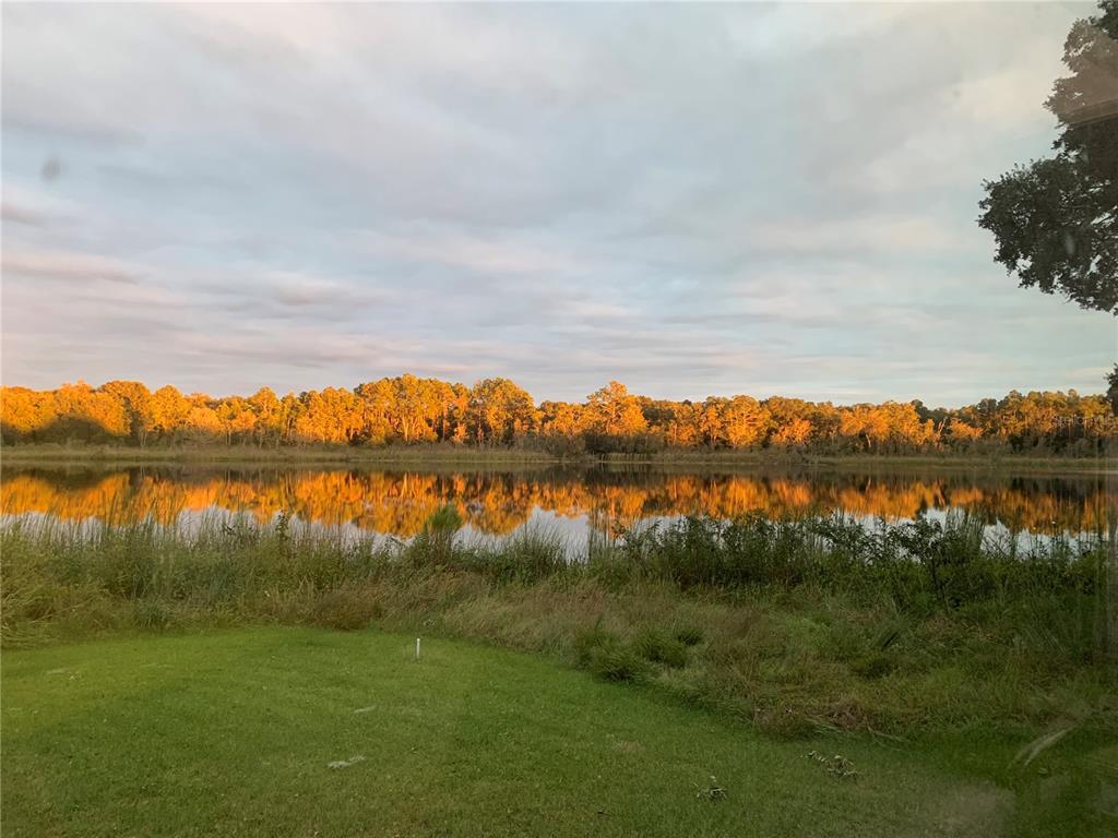 A grassy lawn overlooks a calm lake reflecting a line of sunlit trees at sunset — 640 UNION AVENUE, CRESCENT CITY, FL