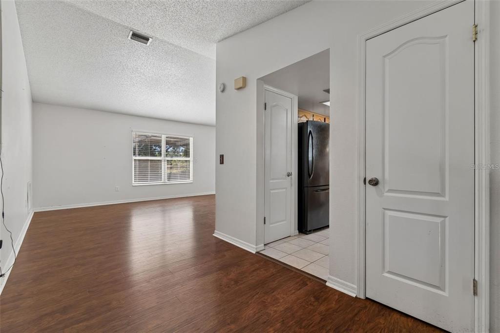 A room with wood-look flooring and a doorway leading to a kitchen with tile floors — 2620 GIANT PLACE, SEFFNER, FL