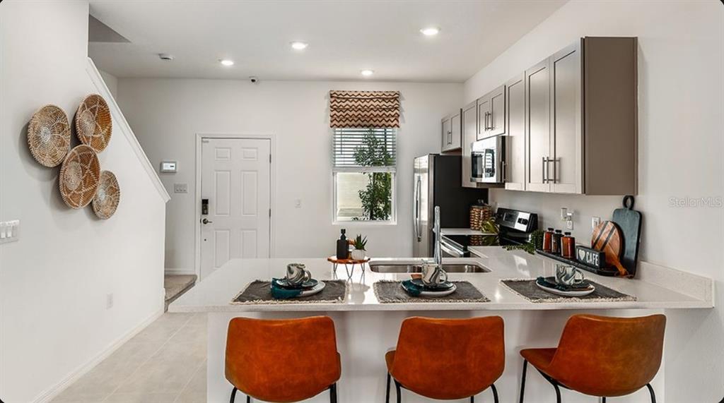 A kitchen features a white island with three orange chairs and gray upper cabinets — 10652 ORBIT TERRACE, SARASOTA, FL