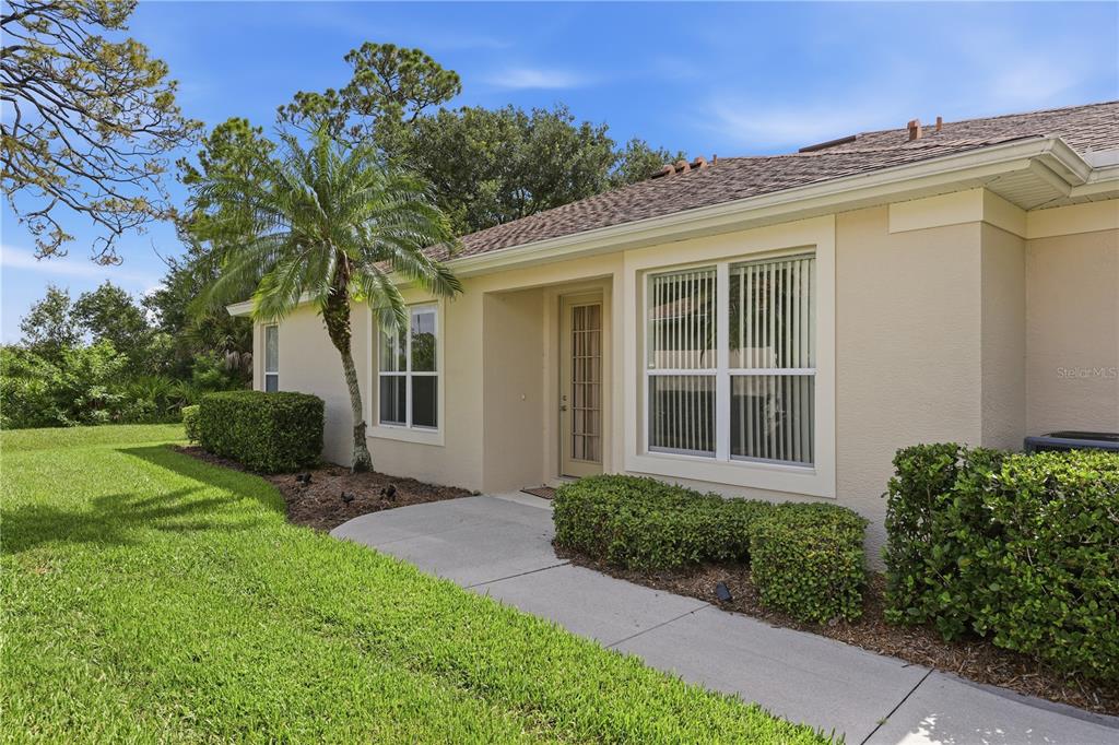 A beige single-story house exterior features a concrete walkway, a small palm tree, and landscaping — 2462 MAGNOLIA CIRCLE, NORTH PORT, FL