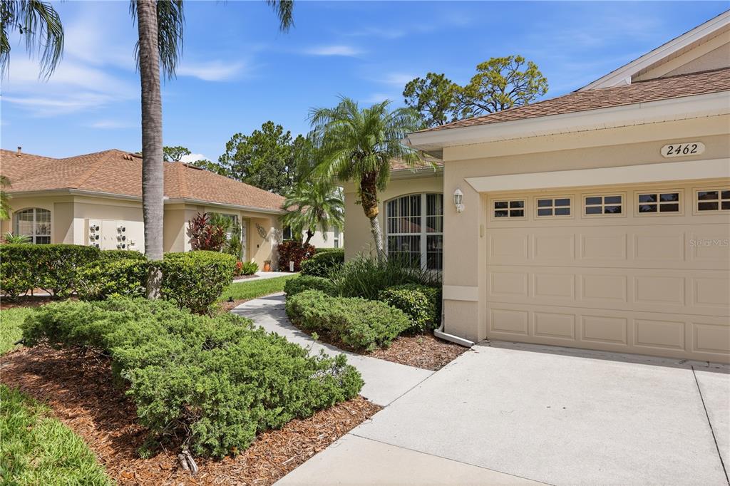 A beige house exterior features a garage, a concrete walkway, and surrounding landscaping — 2462 MAGNOLIA CIRCLE, NORTH PORT, FL