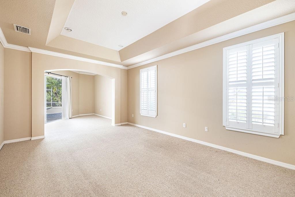 An empty room with beige carpet, tray ceilings, and white plantation shutters on the windows — 5028 ASHINGTON LANDING DRIVE, TAMPA, FL