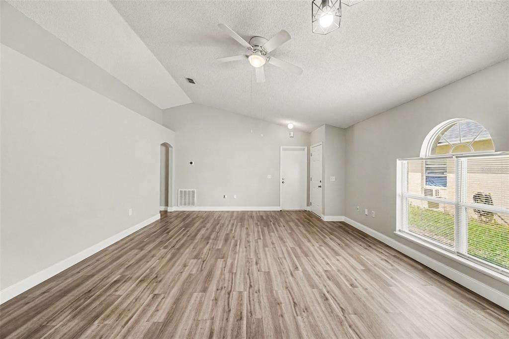 An empty living room features vaulted ceilings, light gray walls, and wood-look laminate flooring — 104 ORION WAY, SANFORD, FL