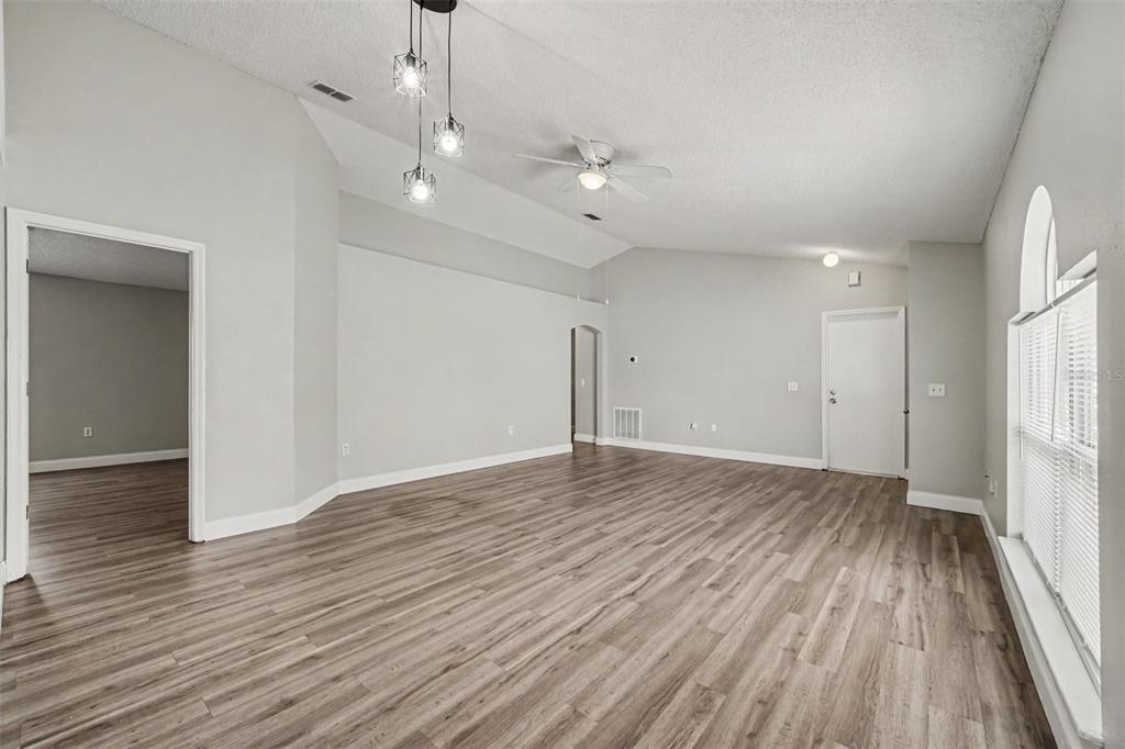 An empty living room features light gray walls, wood-look flooring, a ceiling fan, and pendant lights — 104 ORION WAY, SANFORD, FL