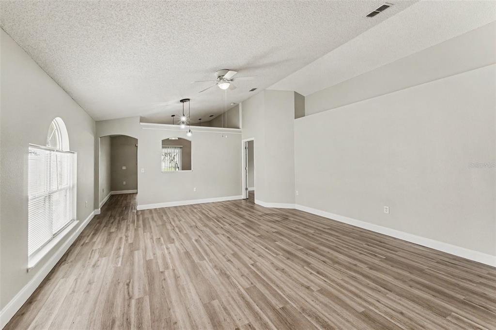 An empty living room features light gray walls, wood-look flooring, and a vaulted ceiling — 104 ORION WAY, SANFORD, FL
