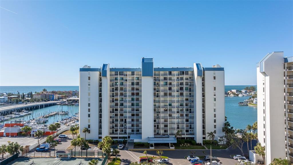 An aerial view shows a multi-story residential building near a marina and the ocean — 9525 BLIND PASS ROAD UNIT 307, ST PETE BEACH, FL