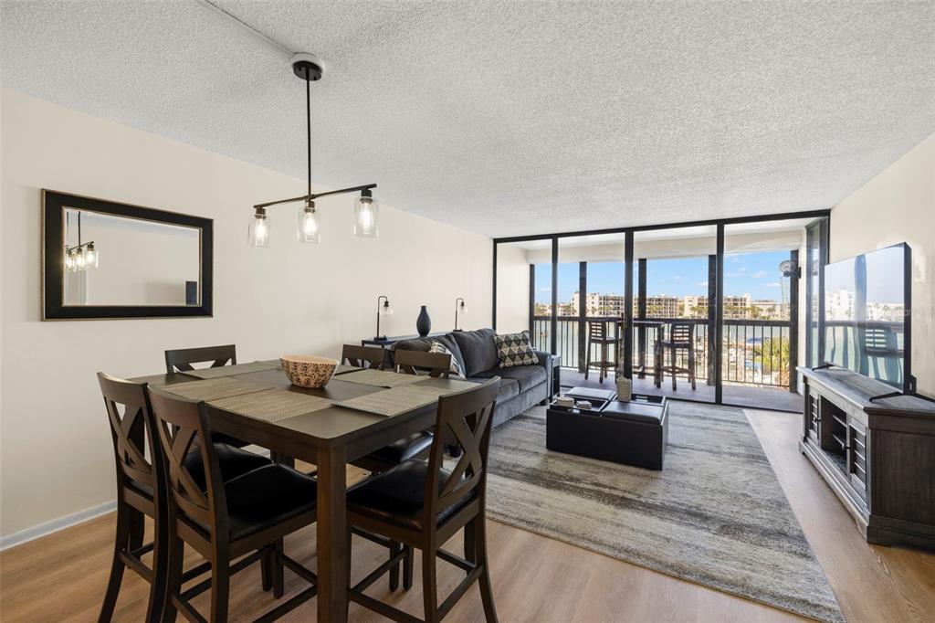 A dining and living area with dark wood furniture, a gray sofa, and a balcony view — 9525 BLIND PASS ROAD UNIT 307, ST PETE BEACH, FL