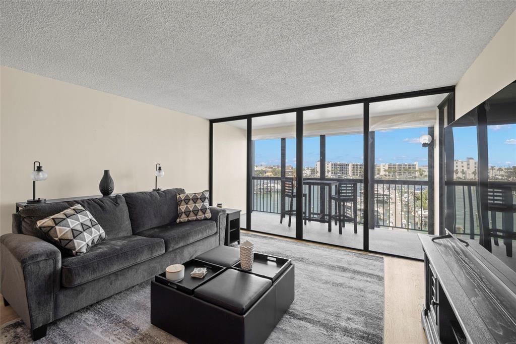 A living room with a dark sofa, ottoman, and sliding glass doors overlooking a marina — 9525 BLIND PASS ROAD UNIT 307, ST PETE BEACH, FL