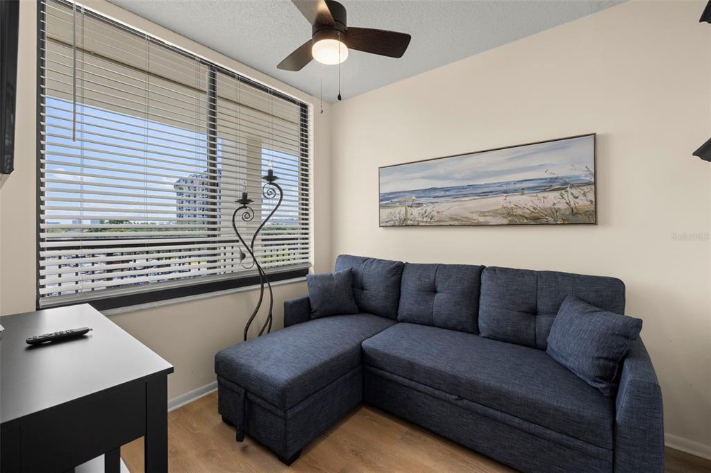 A room features a blue sectional sofa, a desk, a ceiling fan, and window blinds — 9525 BLIND PASS ROAD UNIT 307, ST PETE BEACH, FL