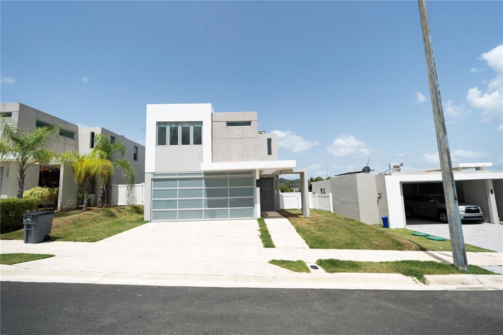 A modern two-story house with a white facade, concrete accents, and a glass garage door — Calle 13 UNIT 134, GUAYNABO, PR