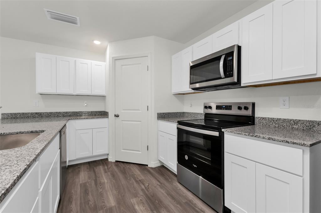 A kitchen features white cabinets, granite countertops, stainless steel appliances, and wood-look flooring — 1040 SHERWIN STREET, PORT CHARLOTTE, FL