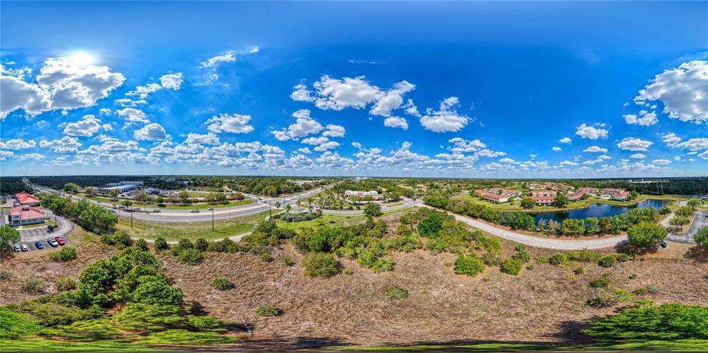 An aerial panoramic view shows a grassy field, a pond, and nearby commercial buildings — 2487 SYCAMORE STREET, NORTH PORT, FL