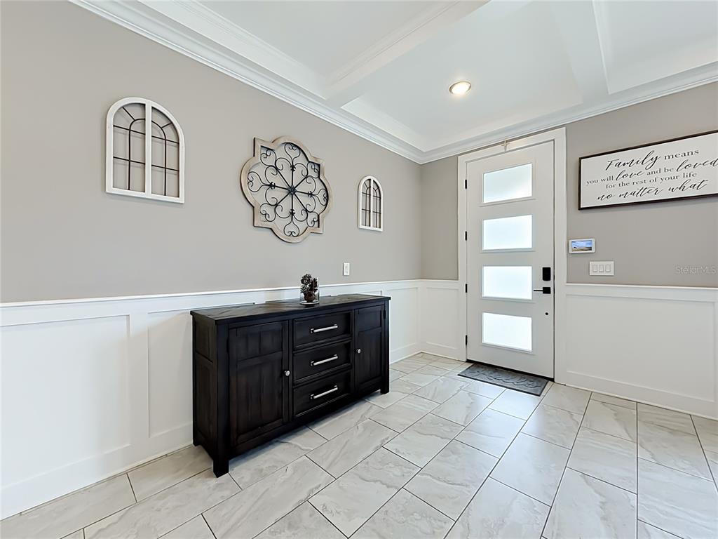A foyer features a dark wood console table, white wainscoting, and a modern front door — 1515 BLUE HORIZON DRIVE, CLERMONT, FL