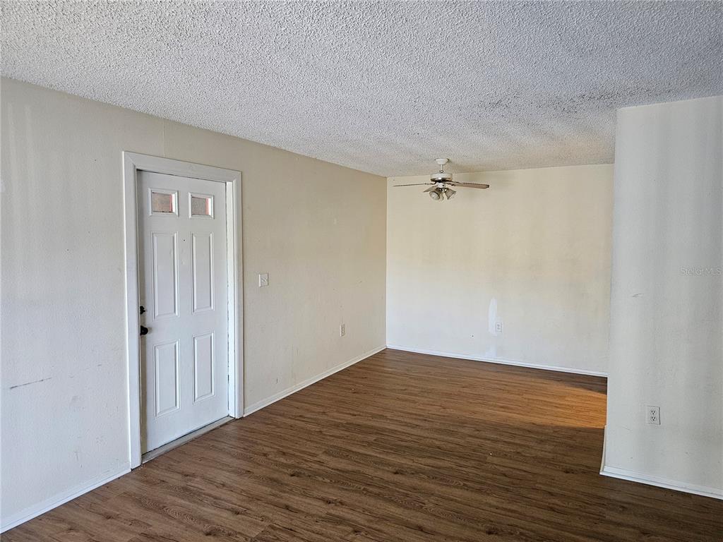 An empty room features wood-look flooring, a ceiling fan, and a white entry door — 5400 26TH STREET W UNIT E80, BRADENTON, FL