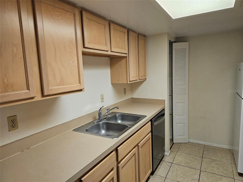 A kitchen features light wood cabinets, a laminate countertop, a double sink, and tile flooring — 5400 26TH STREET W UNIT E80, BRADENTON, FL