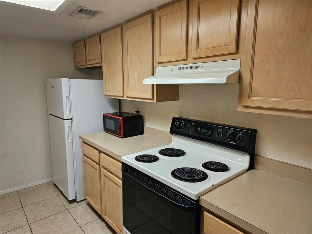 A kitchen features light wood cabinets, a white refrigerator, and a black electric range — 5400 26TH STREET W UNIT E80, BRADENTON, FL