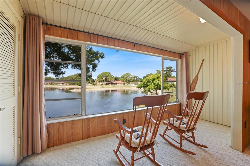 A sunroom with wood-paneled walls and two rocking chairs overlooks a lake through large windows — 4438 NARRAGANSET TRAIL UNIT 98A, SARASOTA, FL