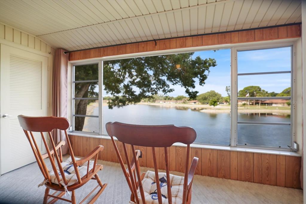 A sunroom with wood-paneled walls and two rocking chairs overlooking a lake — 4438 NARRAGANSET TRAIL UNIT 98A, SARASOTA, FL