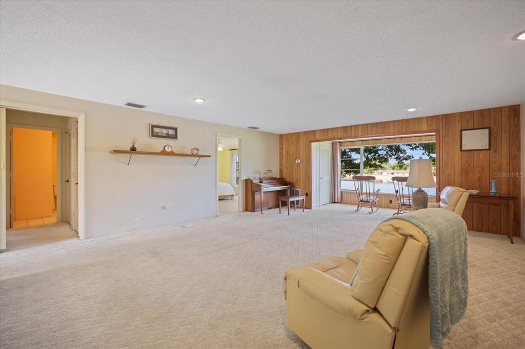 A carpeted living room features wood-paneled walls, a piano, and a large window overlooking water — 4438 NARRAGANSET TRAIL UNIT 98A, SARASOTA, FL