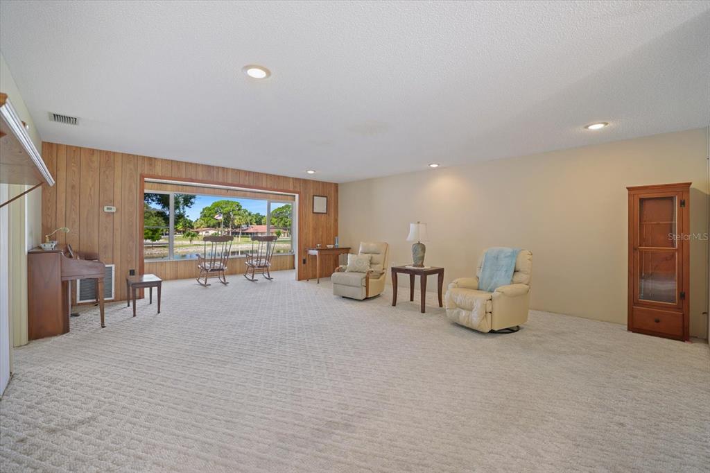 A living room features wood-paneled walls, a large window overlooking a pond, and beige carpet — 4438 NARRAGANSET TRAIL UNIT 98A, SARASOTA, FL