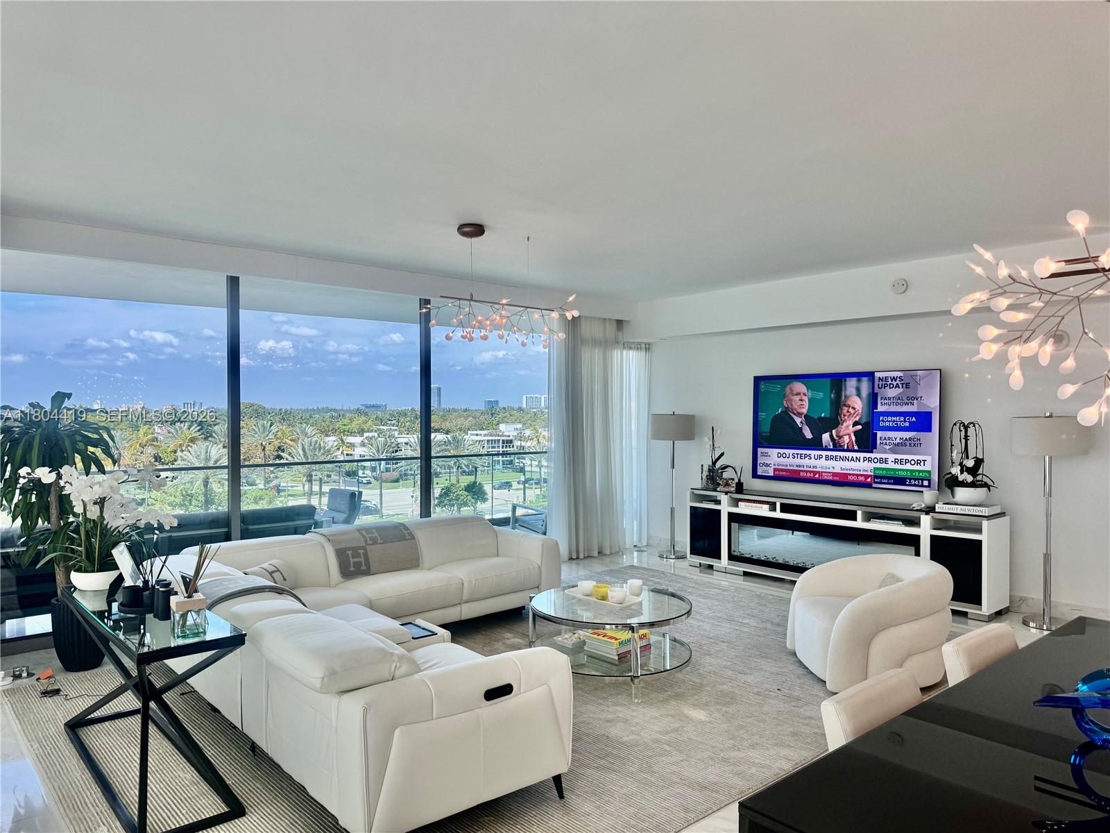 A modern living room features a white sectional sofa, glass coffee table, and floor-to-ceiling windows — 10201 Collins Ave # 511, Bal Harbour FL 33154, BAL HARBOUR, FL