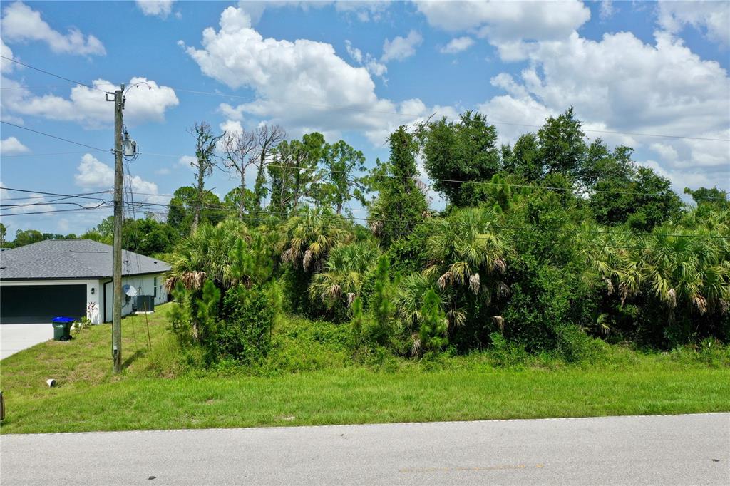 A vacant, wooded lot sits next to a modern house under a cloudy blue sky — NORDENDALE BOULEVARD, NORTH PORT, FL