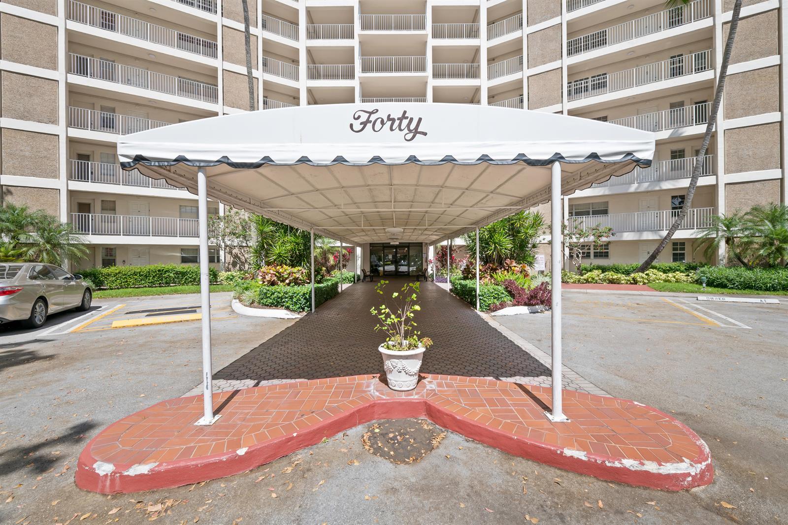 An exterior view of a residential building entrance featuring a covered driveway and awning — 3051 N Course Drive # 211, Pompano Beach FL 33069, POMPANO BEACH, FL