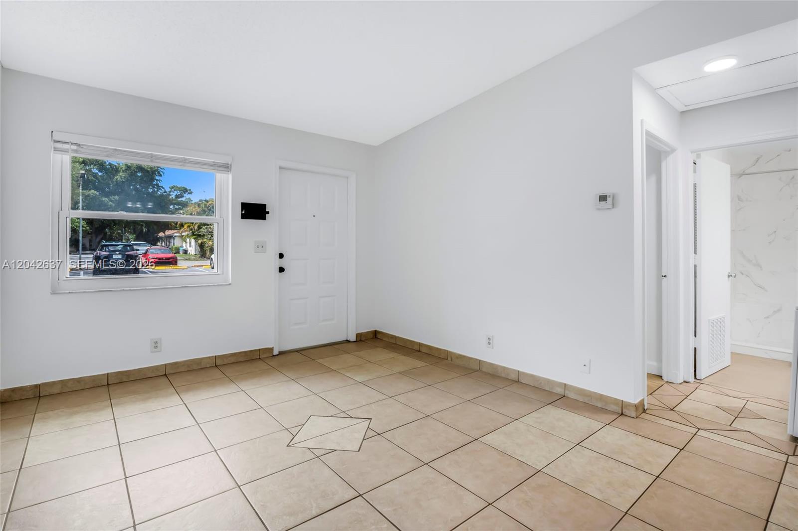This room features white walls, tan tile flooring, a window, and a white entry door — 5020 Sanctuary Way # C, West Palm Beach FL 33417, WEST PALM BEACH, FL