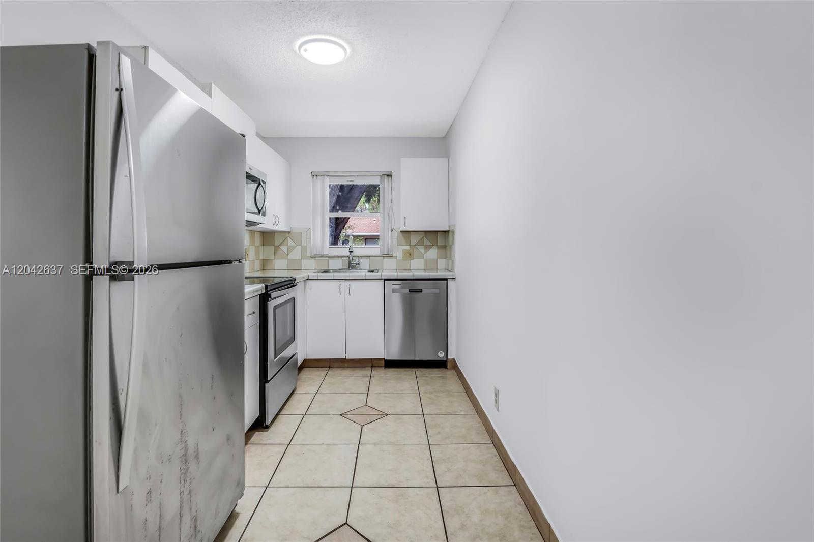 A galley kitchen features stainless steel appliances, white cabinets, and light-colored tile flooring — 5020 Sanctuary Way # C, West Palm Beach FL 33417, WEST PALM BEACH, FL