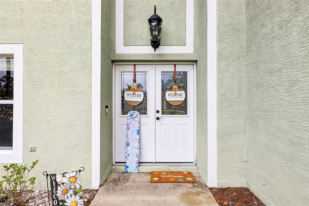 A light green house exterior features white double front doors with spring-themed decorations — 17 PINELL LANE, PALM COAST, FL