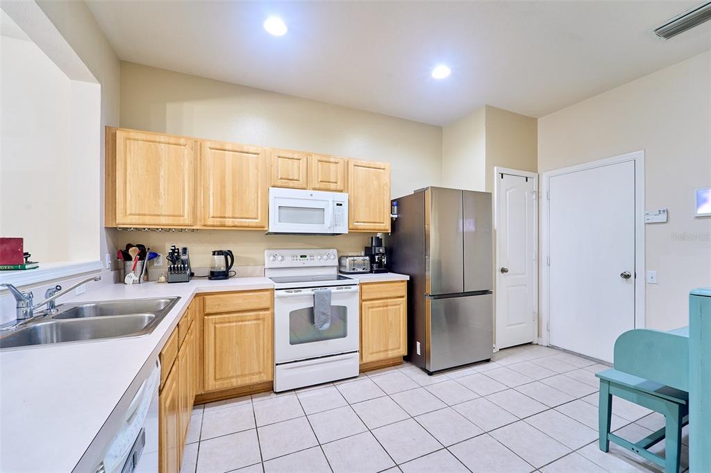 A kitchen features light wood cabinets, white appliances, a stainless steel refrigerator, and tile flooring — 5014 POND RIDGE ROAD, RIVERVIEW, FL