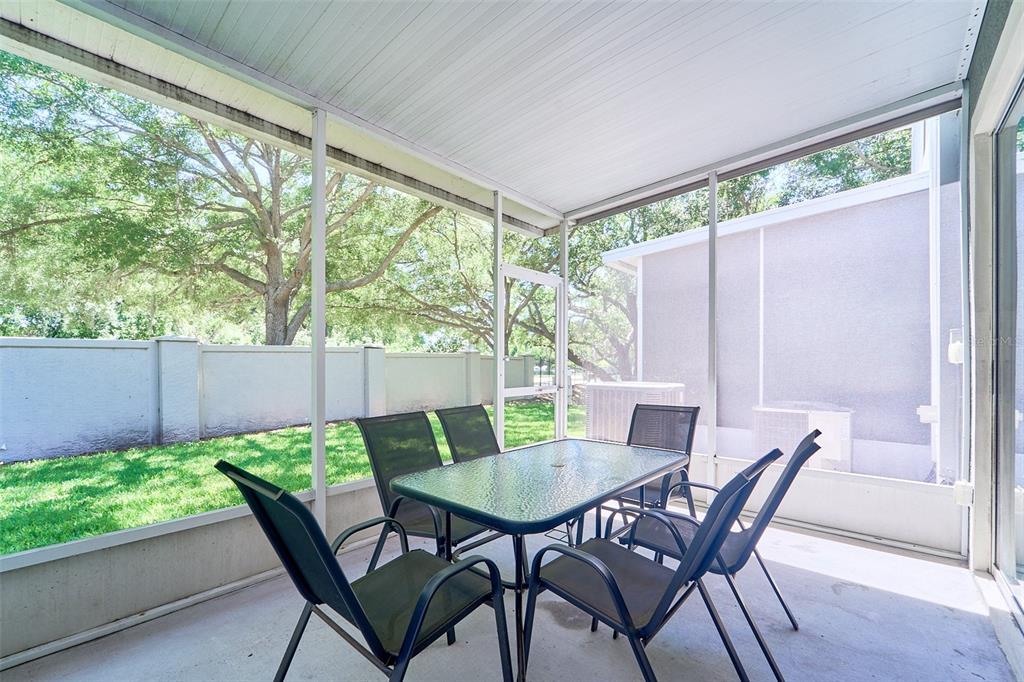 A screened-in patio features a glass-top dining table with chairs overlooking a grassy yard — 5014 POND RIDGE ROAD, RIVERVIEW, FL