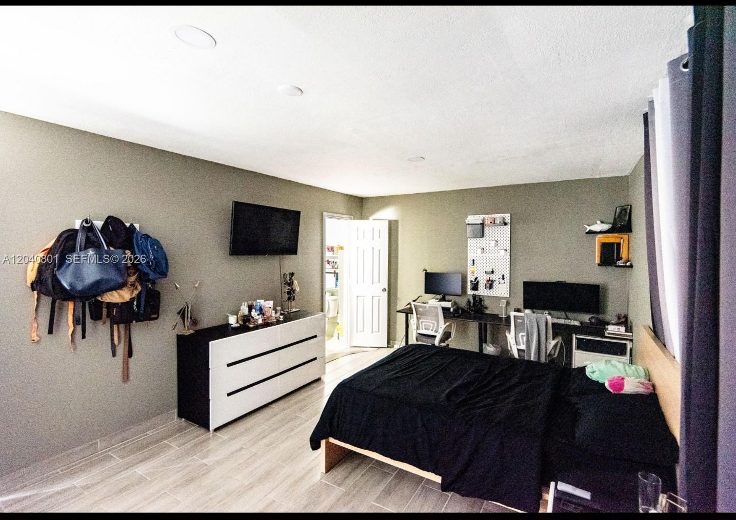 An empty room features gray walls, wood-look tile flooring, a white door, and a wall-mounted AC — 359 W 12th St # 3, Hialeah FL 33010, HIALEAH, FL