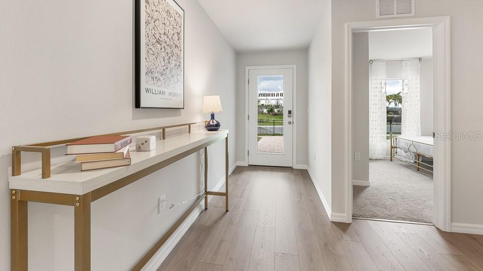 A hallway with light wood flooring, a console table, and a doorway leading to a bedroom — 12419 HOPSCOTCH AVENUE, PARRISH, FL