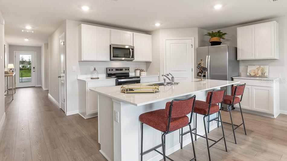 A modern kitchen features white cabinetry, a central island with bar seating, and stainless appliances — 12419 HOPSCOTCH AVENUE, PARRISH, FL