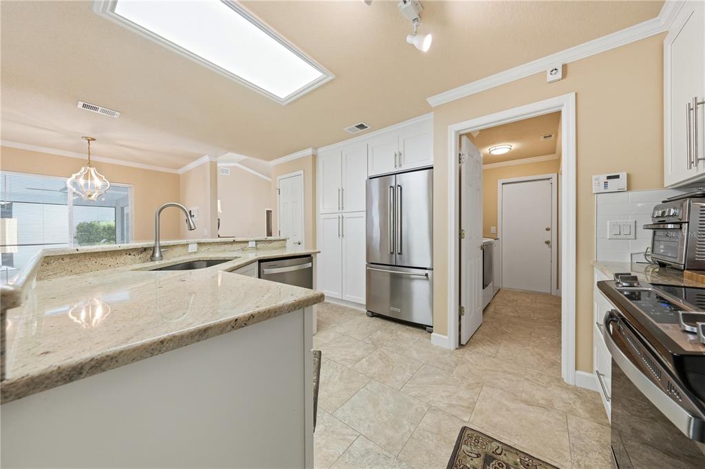 A kitchen features white cabinets, stainless steel appliances, granite countertops, and light-colored tile flooring — 2622 MAYWOOD STREET, EUSTIS, FL