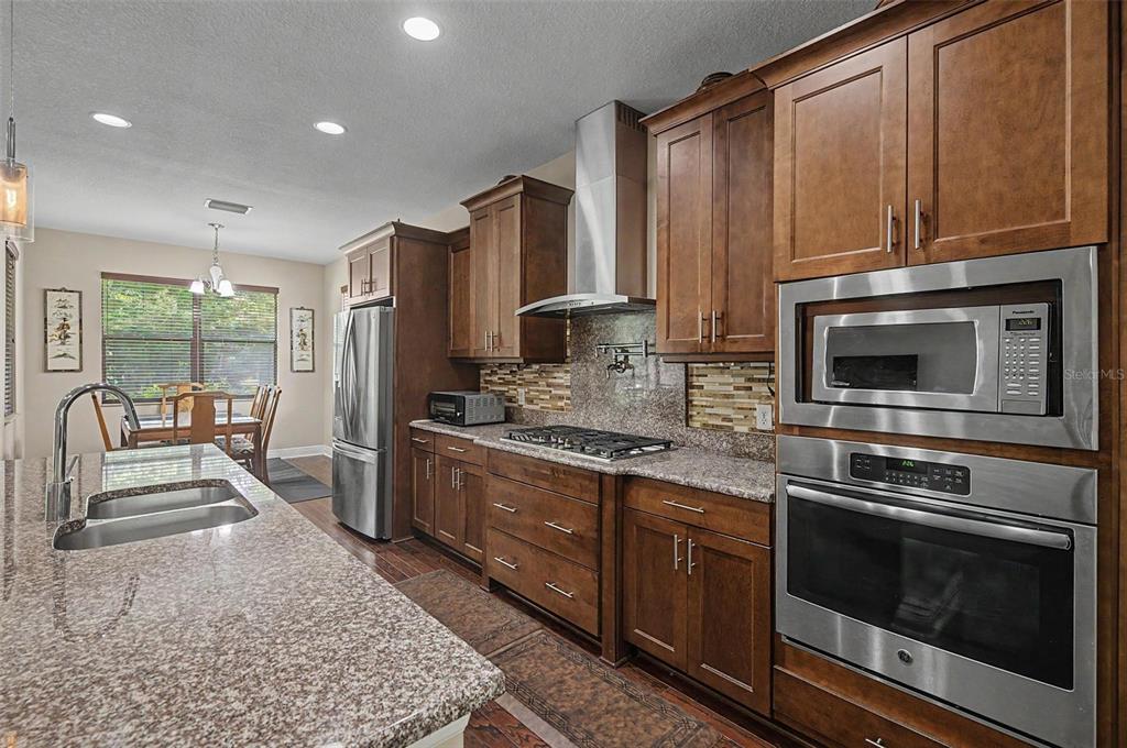 A kitchen features dark wood cabinets, granite countertops, stainless steel appliances, and a dining area — 2234 HIGHWOOD COURT, DUNEDIN, FL