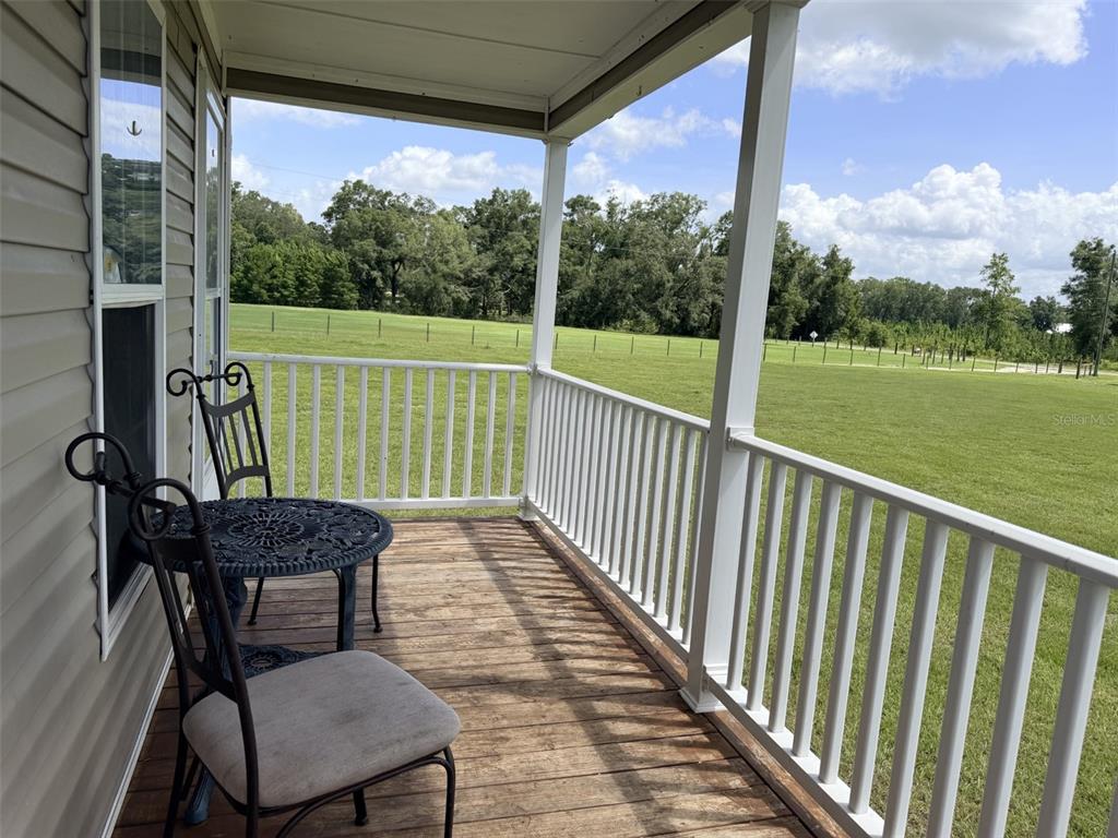 A covered wooden porch features a small bistro set overlooking a large grassy field — 628 NE 816 AVENUE, OLD TOWN, FL