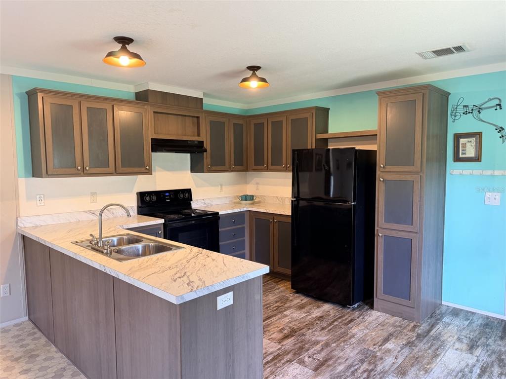 A kitchen features two-tone cabinets, marble-look countertops, a black refrigerator, and light blue walls — 628 NE 816 AVENUE, OLD TOWN, FL