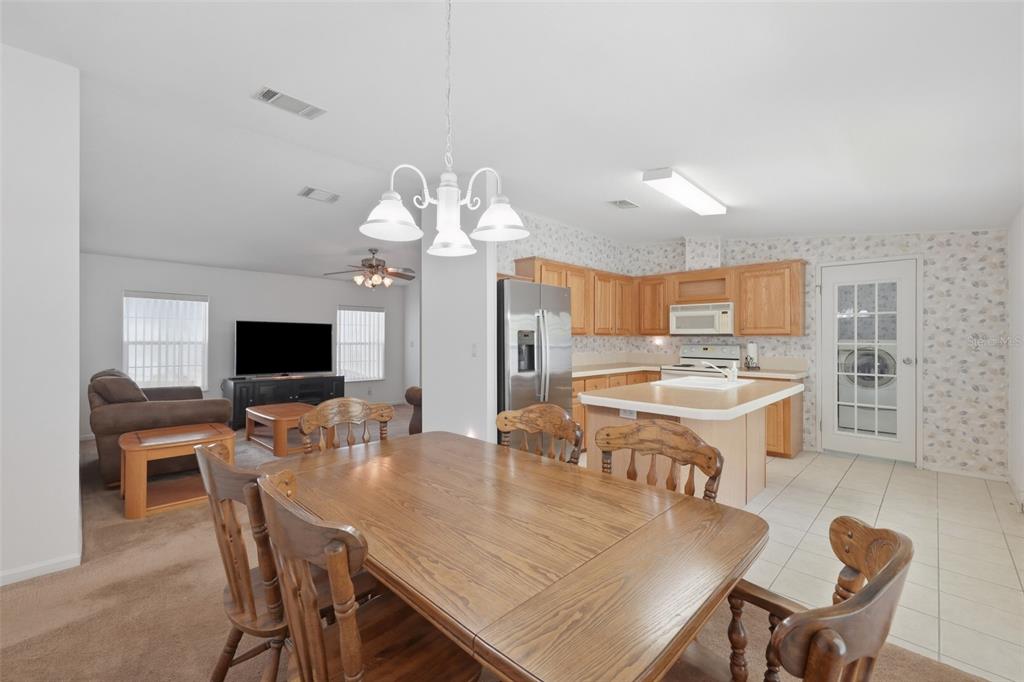 An open-concept kitchen and dining area with wooden cabinets, a central island, and carpeted flooring — 82221 F STREET N UNIT 221, PINELLAS PARK, FL