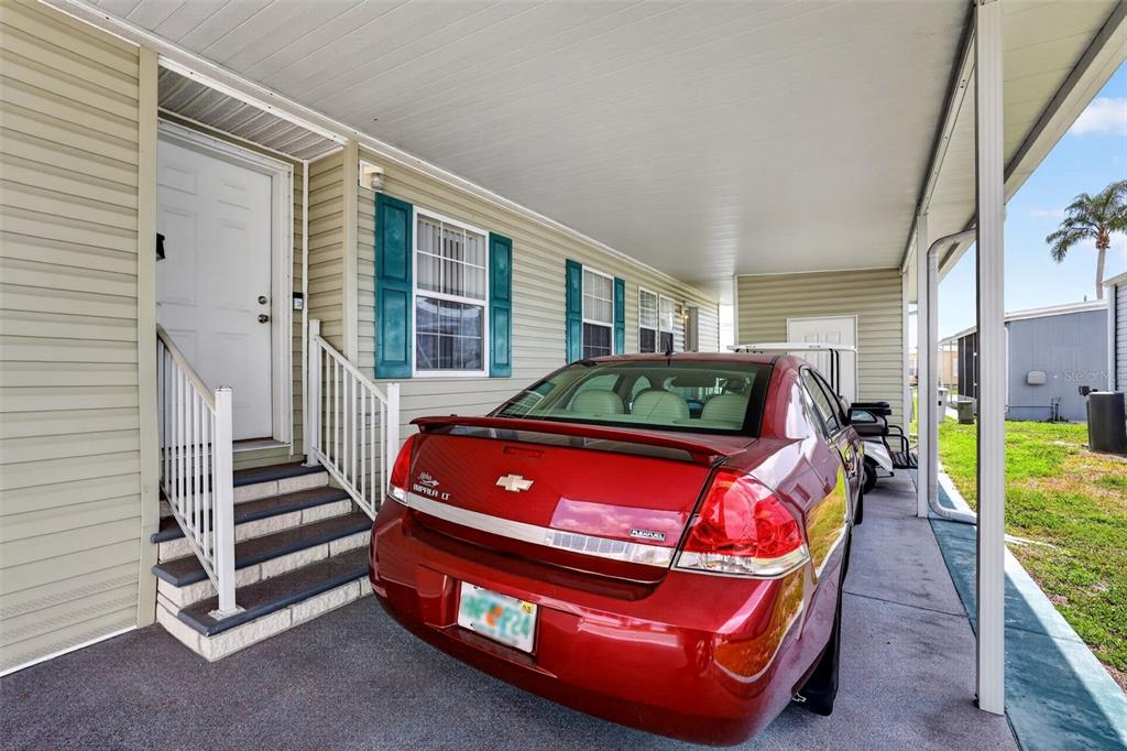 A red sedan is parked under a carport next to a house with beige siding — 82221 F STREET N UNIT 221, PINELLAS PARK, FL