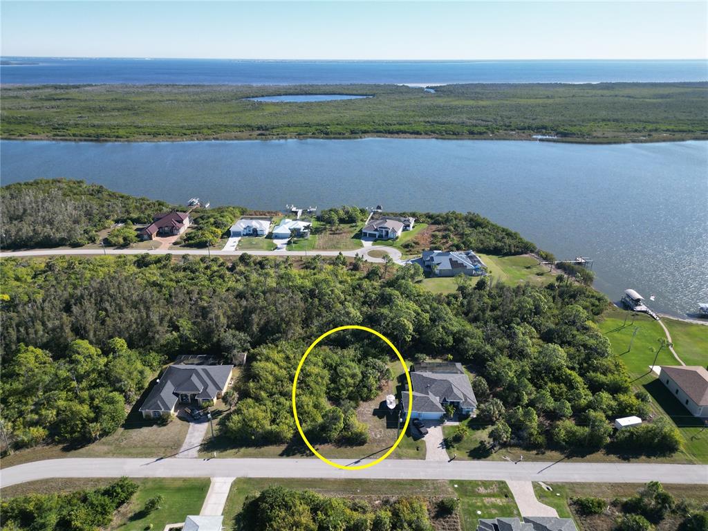 An aerial view shows a vacant, tree-covered lot situated between two houses on a residential street — 9558 SHELBURNE CIRCLE, PORT CHARLOTTE, FL