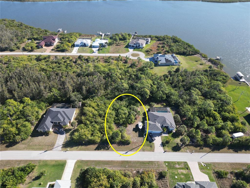 An aerial view shows a vacant, wooded residential lot situated between two houses near water — 9558 SHELBURNE CIRCLE, PORT CHARLOTTE, FL