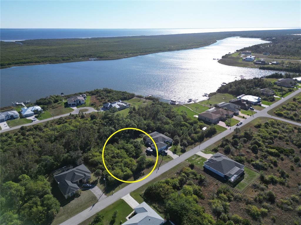 An aerial view shows a vacant, wooded residential lot circled in yellow near a waterfront — 9558 SHELBURNE CIRCLE, PORT CHARLOTTE, FL